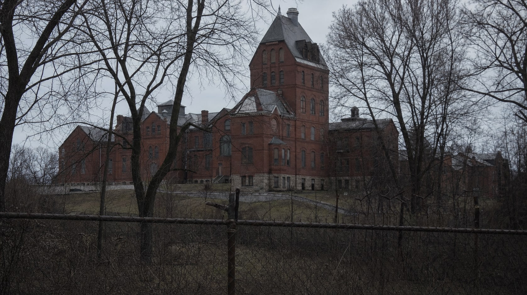 A red-brick institutional hospital campus viewed through winter trees and a fence, representing the St. Elizabeths geography.