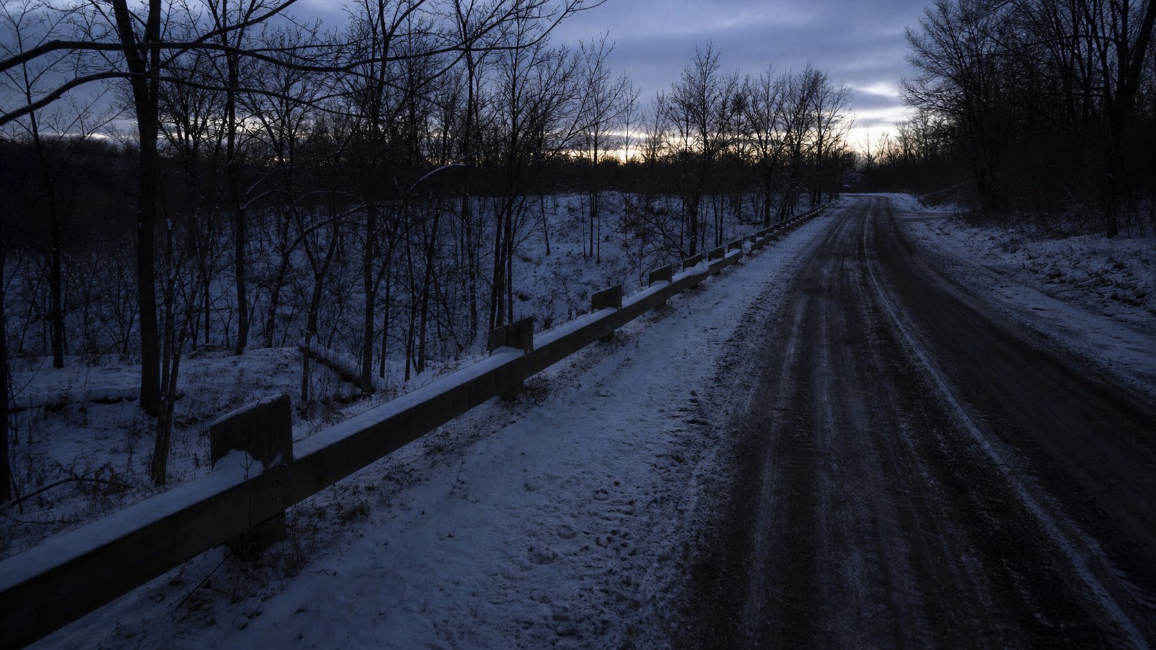 A remote snow-covered Illinois road with a low guardrail at winter twilight, representing the German Church Road discovery area.