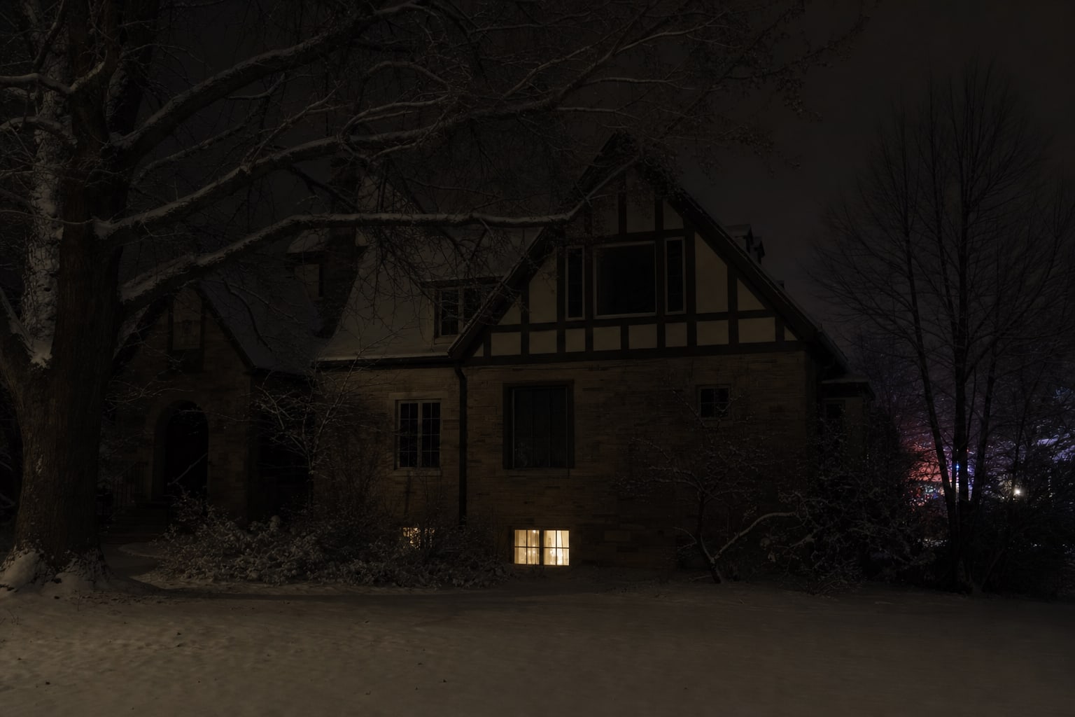 A Tudor-style Boulder home at night with a basement window glowing in the snow, representing the Ramsey house.