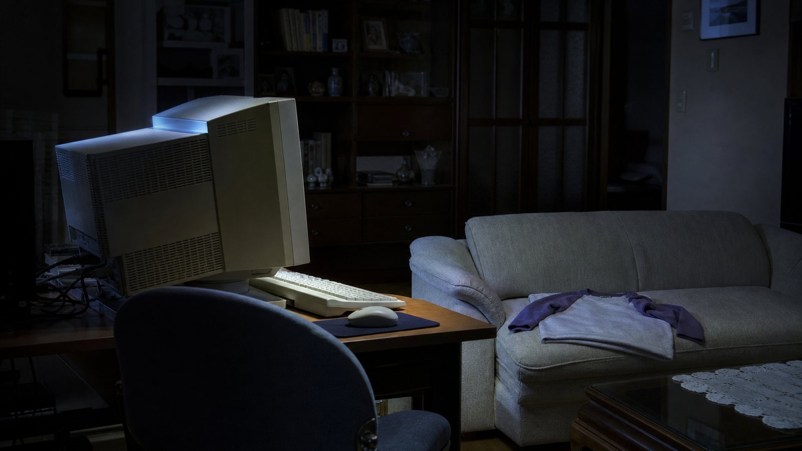A year-2000 desktop computer glowing in a dark Japanese living room with a folded raglan sweatshirt nearby.