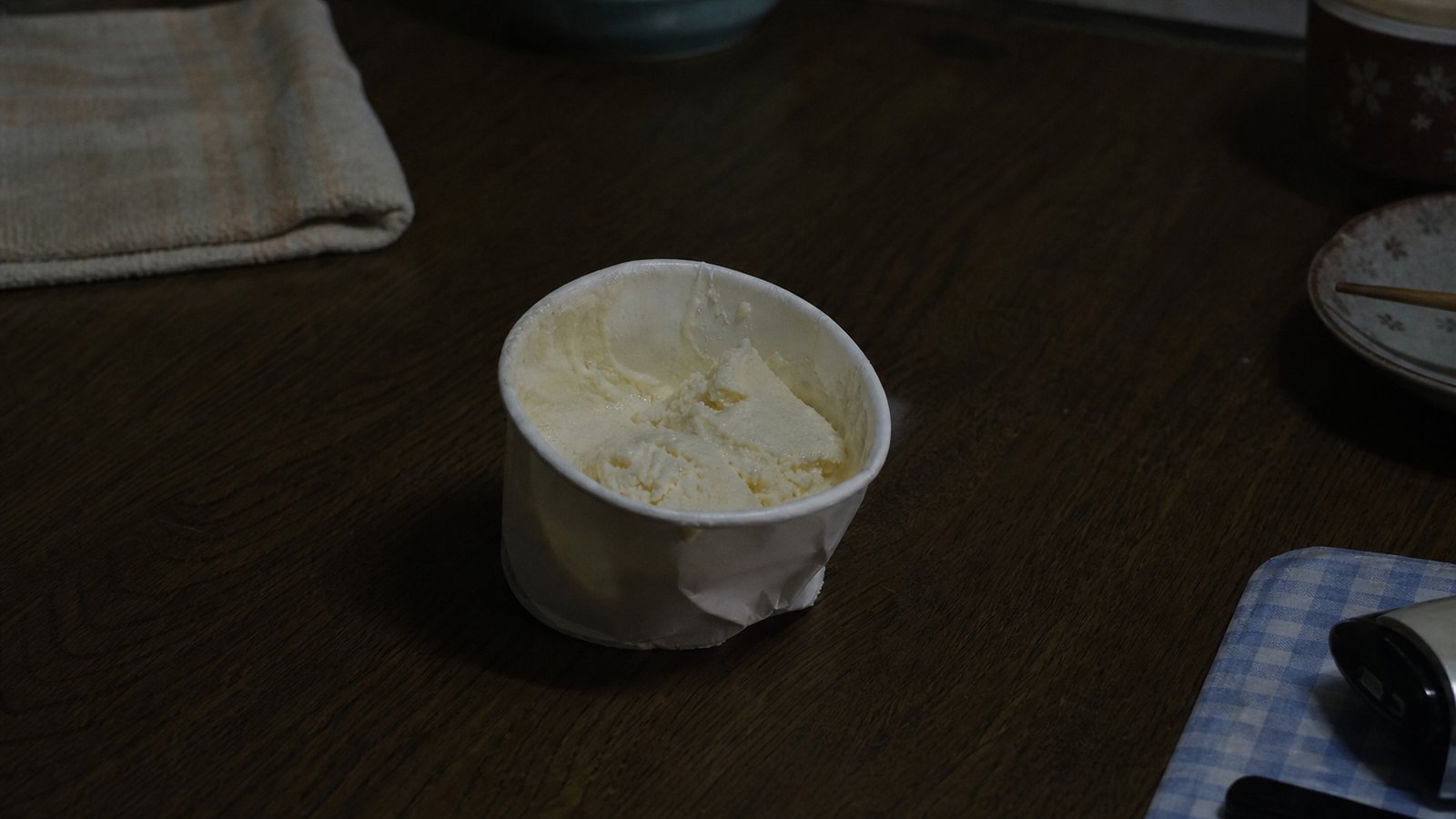 A squeezed cup of vanilla ice cream on a dark kitchen table, representing the unusual post-crime behavior reported in the Setagaya case.