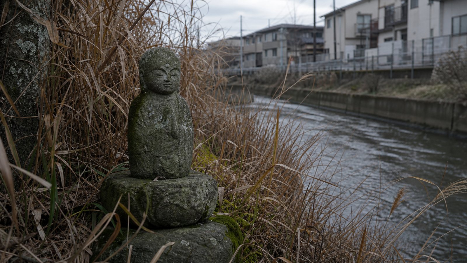 A small weathered Jizo statue near a concrete river channel, representing the later public police appeal in the Setagaya case.