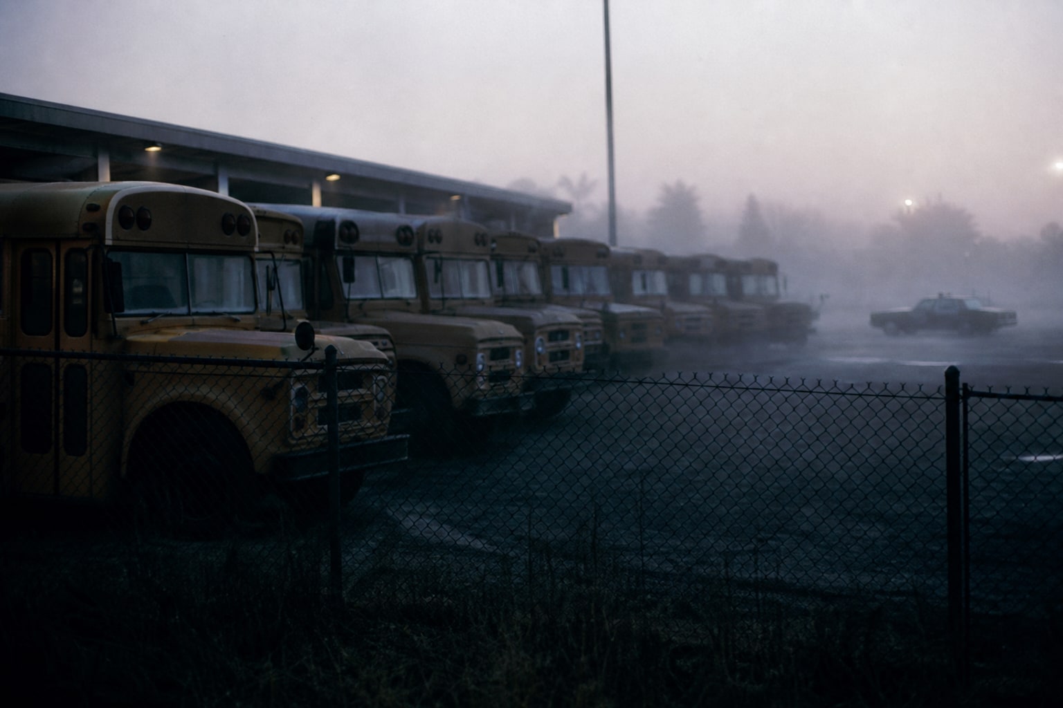 Rows of empty school buses sit behind a fence in fog, representing the public fear caused by Zodiac Killer threats.