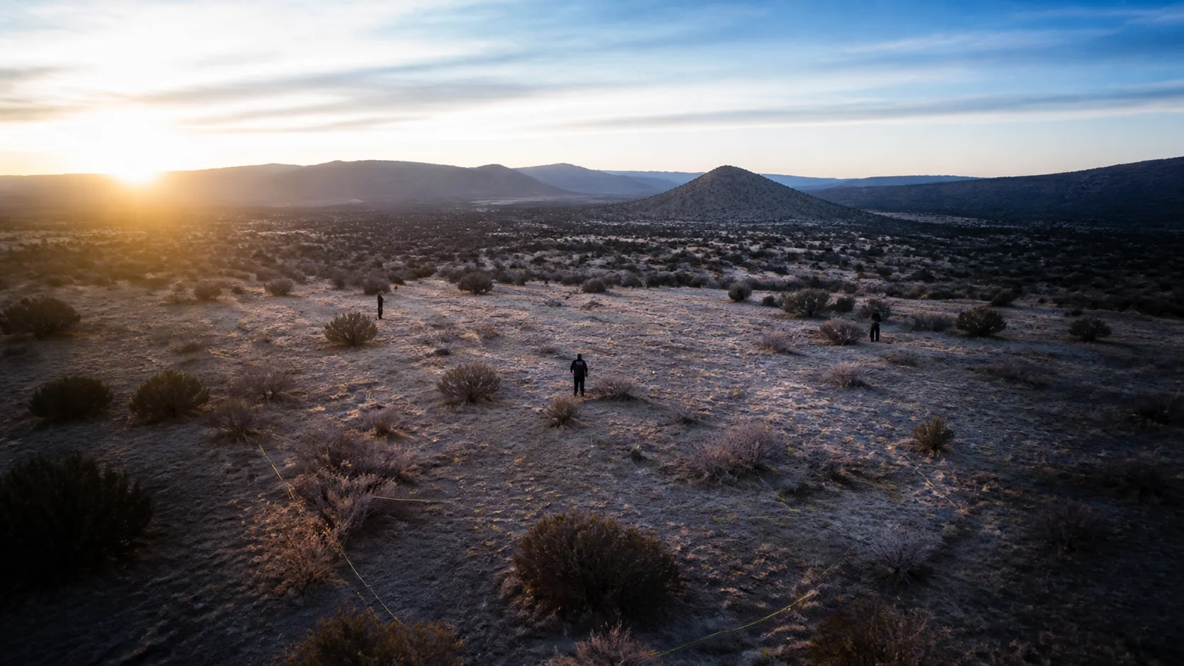 Remote New Mexico desert search grid at first light with distant search personnel