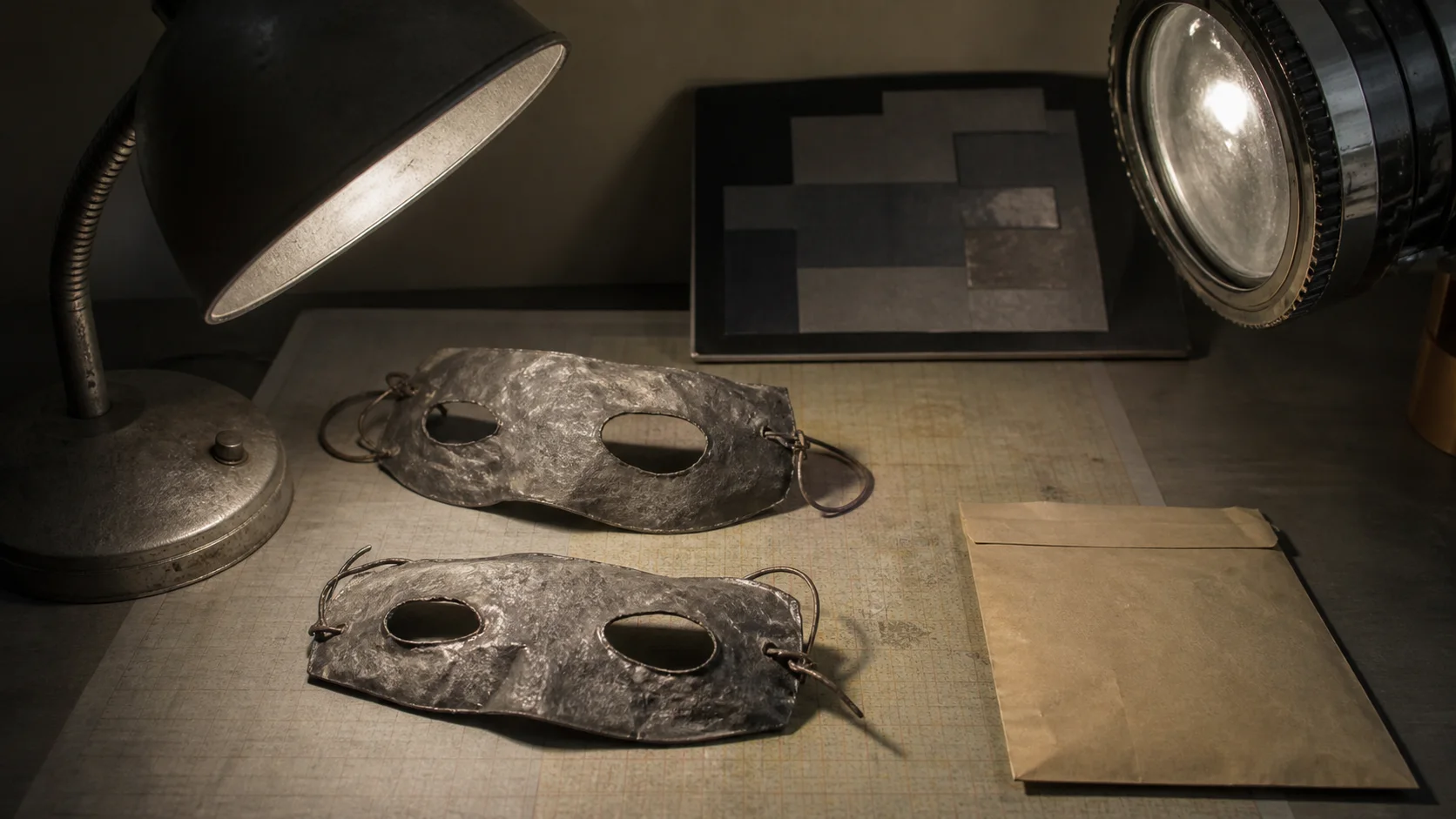 Crude lead eye masks examined beneath a forensic lamp beside an empty evidence envelope