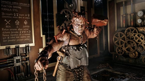 The Hammer from Thir13en Ghosts, a ghost with rusty nails impaled in his body, brandishes a sledgehammer in a workshop with industrial gears and a blackboard of alchemical binding formulas.
