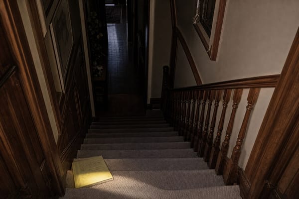 A carpeted staircase with a yellow notepad resting on a lower step, representing the JonBenét Ramsey ransom note.